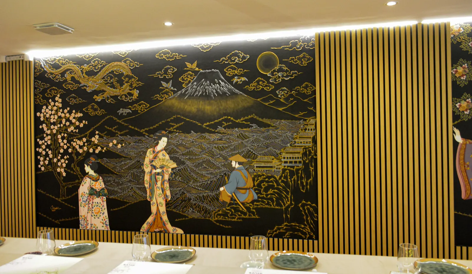 La fresque noire et dorée qui court au-dessus du comptoir : le mont Fuji, un dragon, des geishas