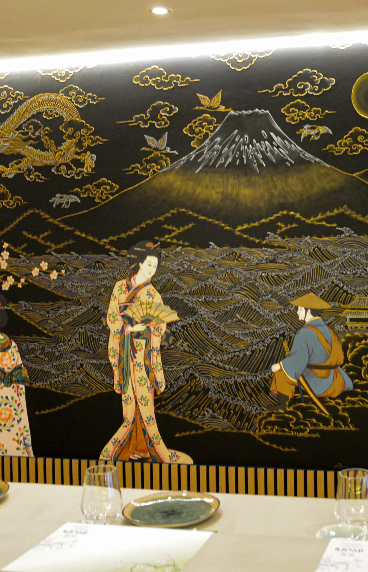 Détail de la fresque noire et dorée : le mont Fuji et une geisha à l’éventail